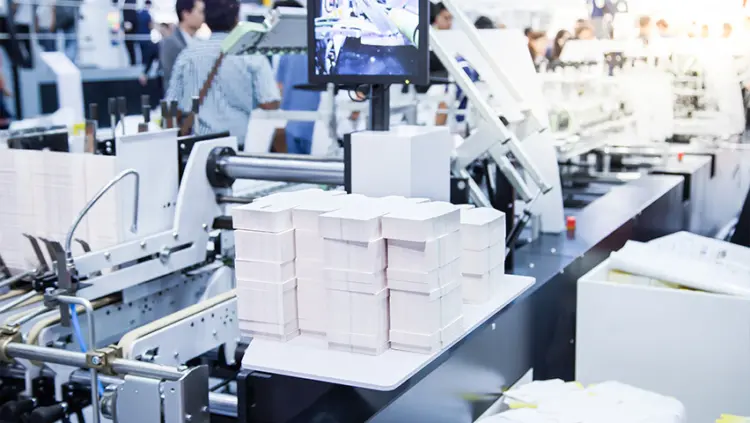 426×240-Westrock A factory interior showing workers operating machinery, focused on their tasks in a busy industrial environment.
