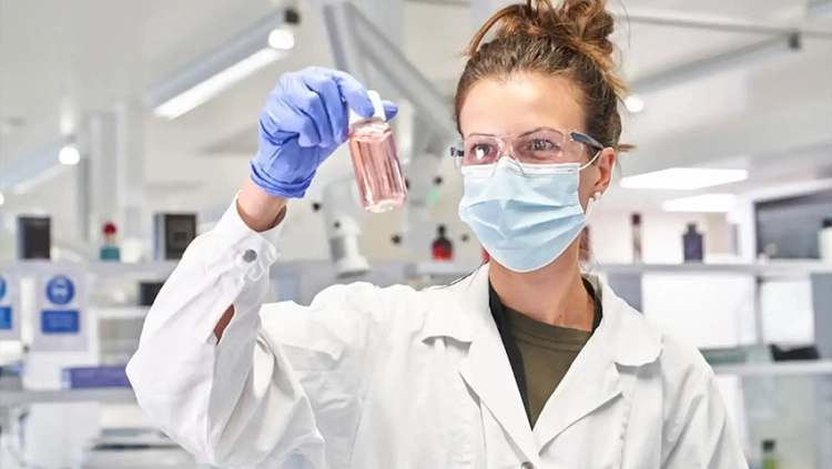426×240-coty A woman in a lab coat holds a test tube, showcasing her work in a scientific laboratory setting.