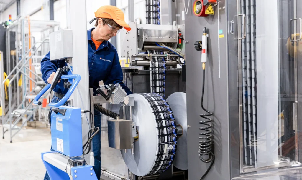 A woman in an orange shirt and blue hat operates a machine, focused on his task.