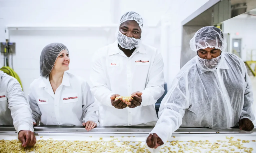 A group of people in white coats gathers around a conveyor belt, observing the items moving along the production line.