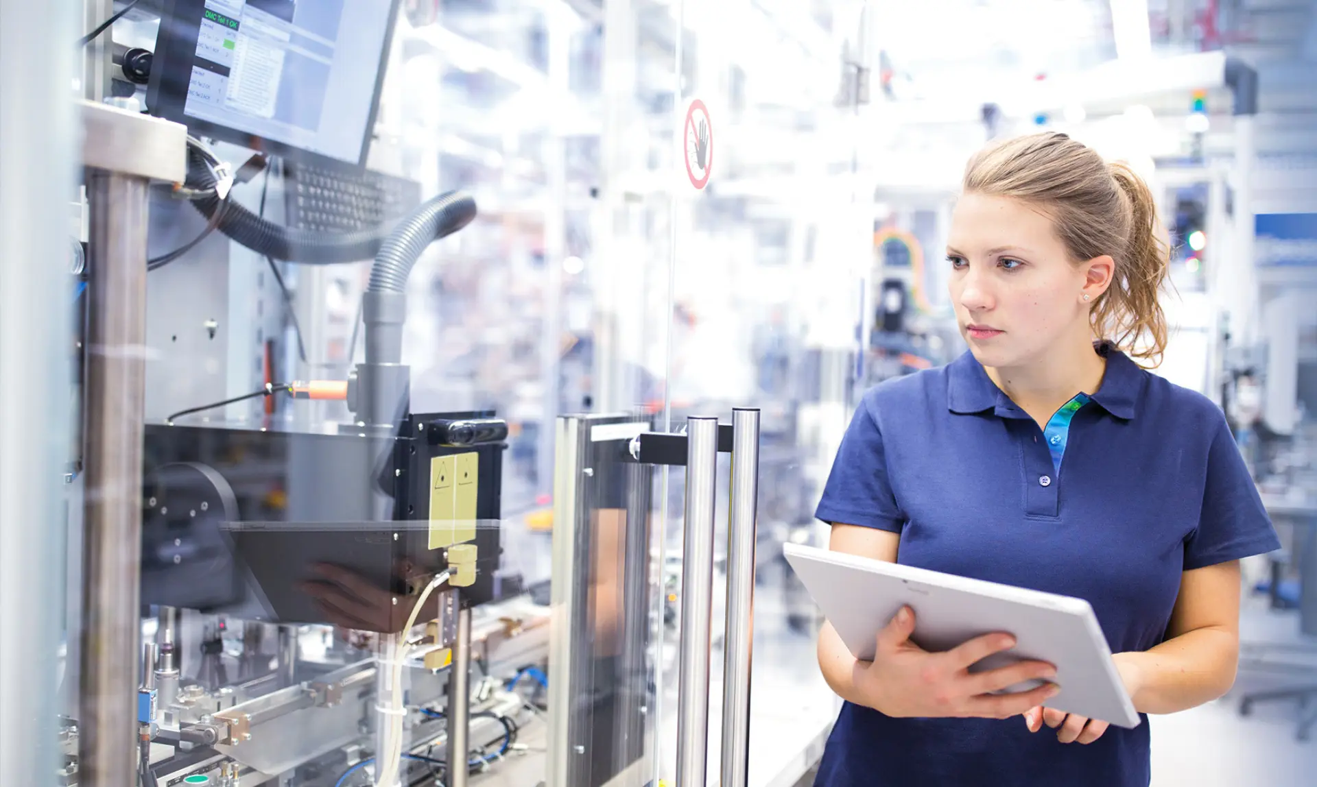 A woman wearing a blue shirt is holding a tablet computer in her hands, looking focused and engaged.