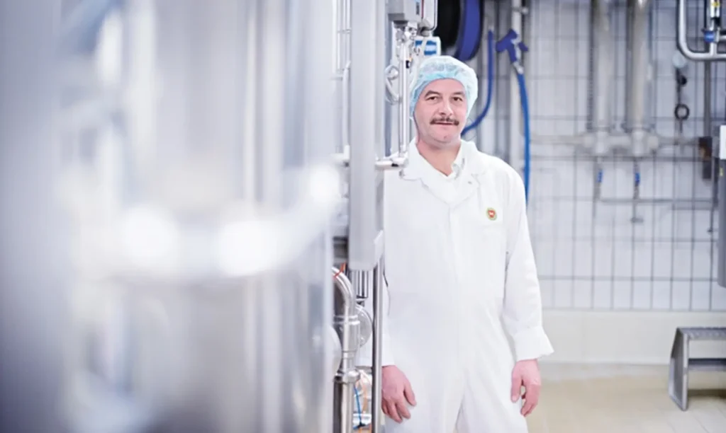 A man in a white lab coat stands in a factory, overseeing operations and ensuring quality control.