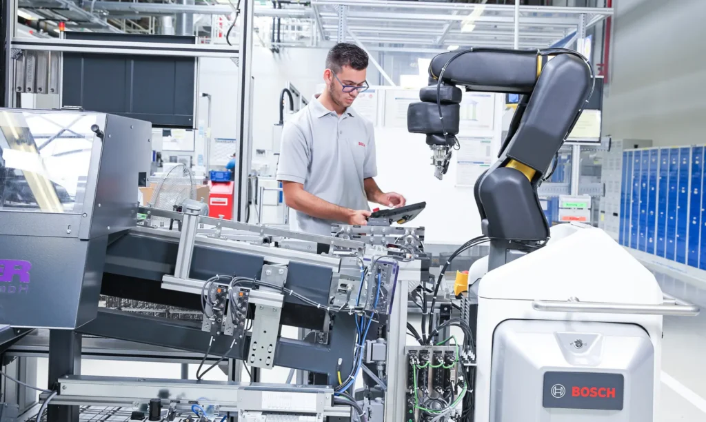 A man operates a machine in a factory, focused on his task amidst industrial equipment and surroundings.