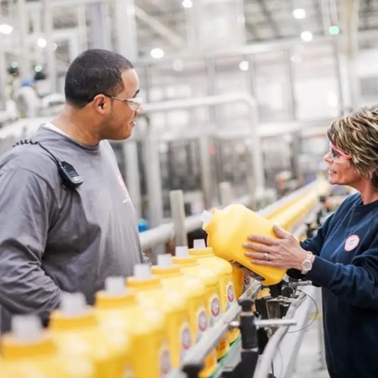 A man and woman stand beside a machine displaying yellow bottles, engaged in conversation about the product.