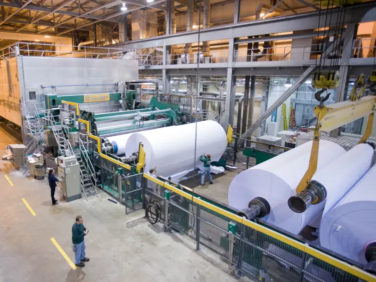 A paper machine in a factory with workers operating machinery and managing production processes.
