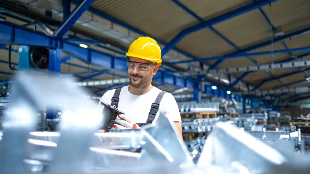 A smiling man in a hard hat operates a machine, showcasing safety and professionalism in a work environment.