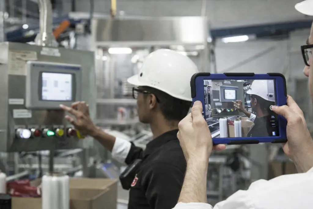 A man wearing a hard hat captures an image of a worker in front of a machine, highlighting features on a work site.