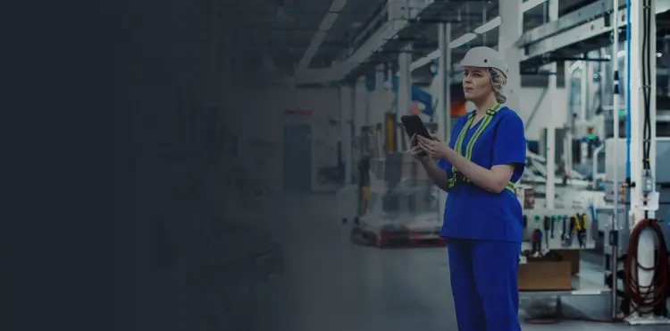 A woman in a blue uniform stands confidently in a factory setting, surrounded by machinery and equipment.
