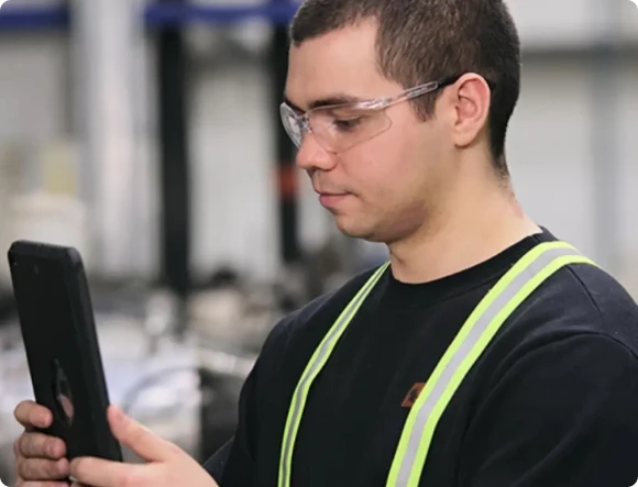 A man wearing safety glasses looking at an iPad in a work environment.