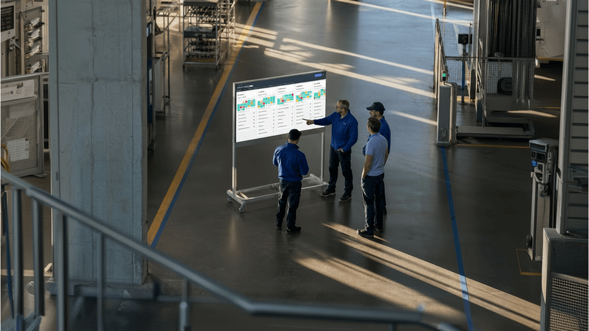 Factory workers reviewing a production dashboard on a digital display.