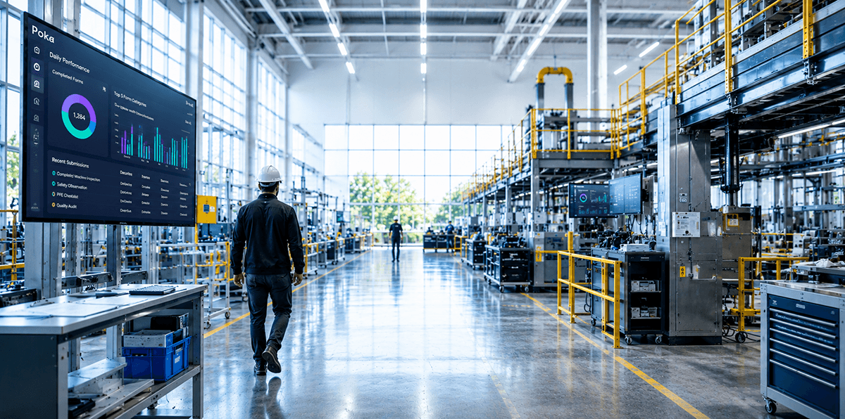 Factory worker walking past digital performance dashboards.
