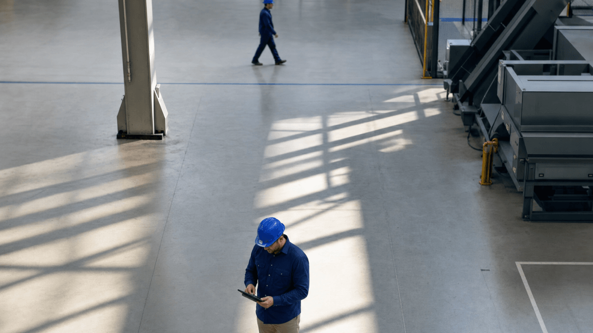 A worker wearing a blue hard hat looking at a mobile device in a factory environment