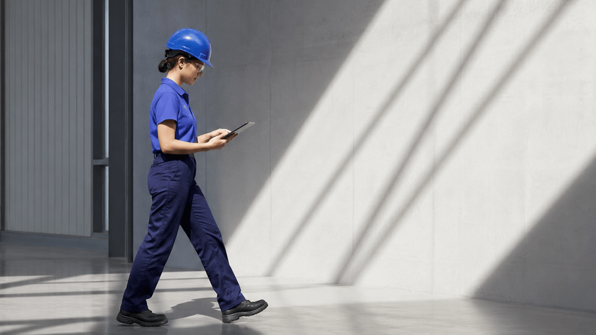 A person wearing a hard hat staring at her tablet and walking